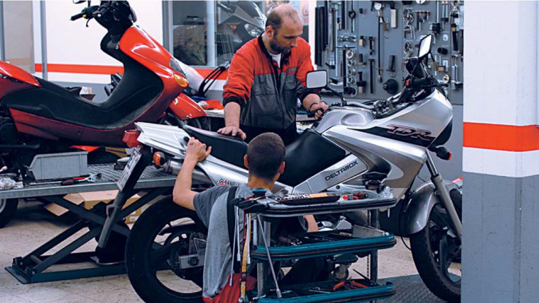 Zdjęcie warsztatu, w którym dwie osoby pracują przy motocyklu.