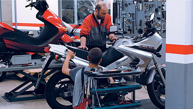 Warsztat samochodowy Zdjęcie warsztatu, w którym dwie osoby pracują przy motocyklu.
